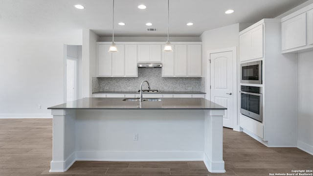 kitchen featuring a kitchen island with sink, stainless steel appliances, hanging light fixtures, and white cabinetry