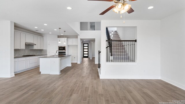 kitchen with white cabinets, a center island with sink, hanging light fixtures, and light hardwood / wood-style flooring