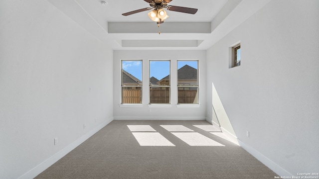 carpeted empty room featuring ceiling fan and a raised ceiling