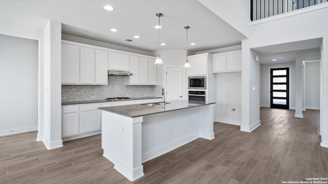 kitchen featuring dark hardwood / wood-style flooring, decorative light fixtures, a center island with sink, stainless steel appliances, and white cabinets