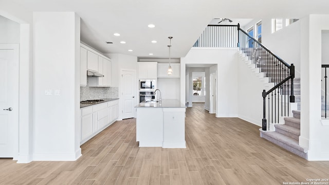 kitchen featuring an island with sink, hanging light fixtures, light hardwood / wood-style floors, and white cabinetry