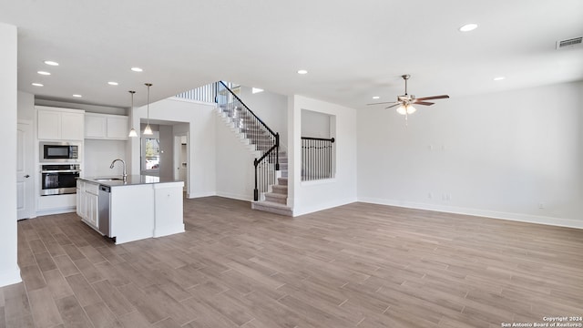 kitchen with a kitchen island with sink, light hardwood / wood-style flooring, sink, white cabinets, and appliances with stainless steel finishes