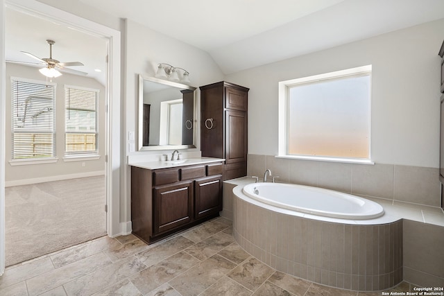 bathroom with ceiling fan, a relaxing tiled tub, vanity, and vaulted ceiling