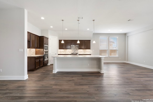 kitchen featuring an island with sink, stainless steel appliances, hanging light fixtures, and dark wood-type flooring