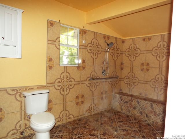 bathroom with a tile shower, vaulted ceiling, tile walls, and toilet