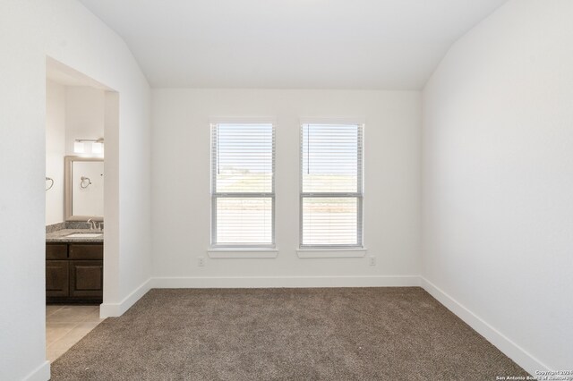 carpeted spare room featuring lofted ceiling and sink