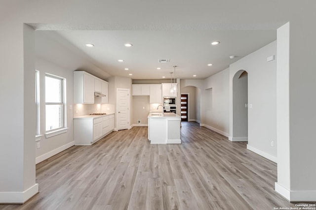 kitchen featuring white cabinetry, a kitchen island with sink, light hardwood / wood-style floors, and decorative light fixtures