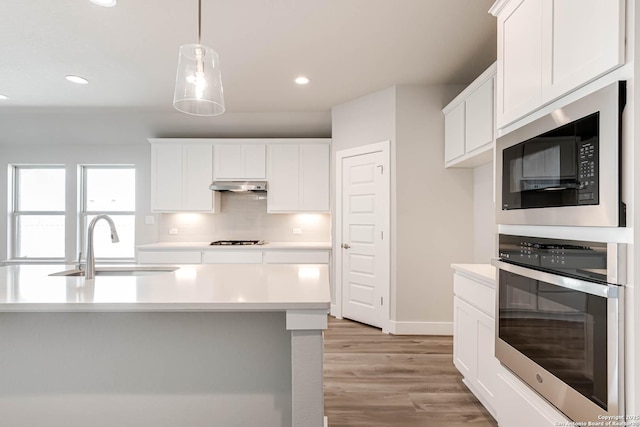 kitchen with built in microwave, sink, white cabinetry, decorative light fixtures, and oven