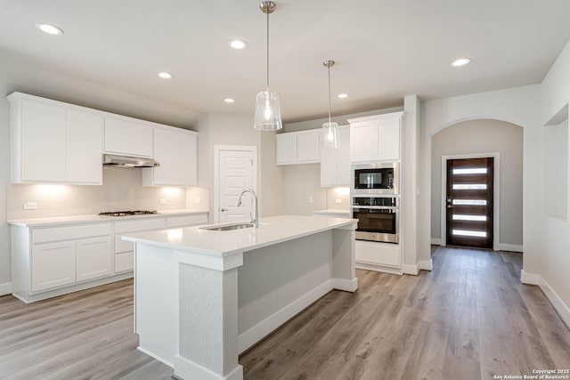 kitchen featuring built in microwave, sink, oven, a kitchen island with sink, and white cabinets