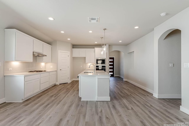 kitchen featuring built in microwave, gas stovetop, a kitchen island with sink, and oven