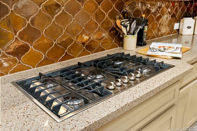 interior details with backsplash, light stone countertops, and stainless steel gas stovetop