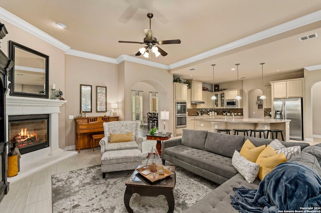 living area with arched walkways, ceiling fan, visible vents, and a glass covered fireplace