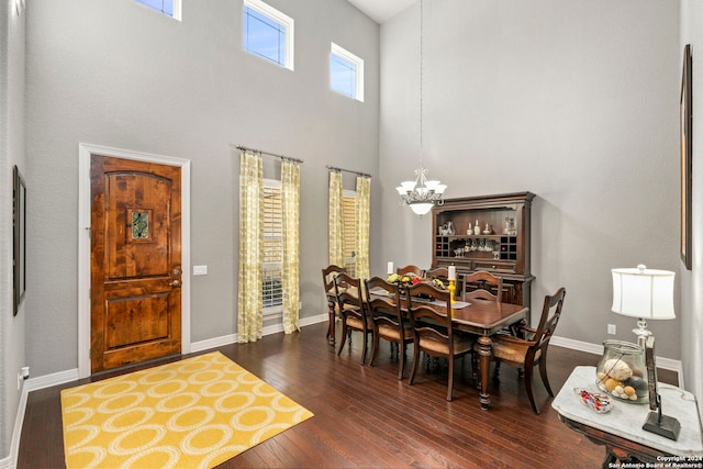 dining space featuring dark wood-type flooring, a healthy amount of sunlight, a towering ceiling, and an inviting chandelier