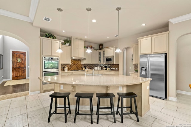 kitchen with hanging light fixtures, a center island with sink, sink, crown molding, and appliances with stainless steel finishes