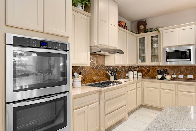 kitchen featuring light stone countertops, appliances with stainless steel finishes, decorative backsplash, and cream cabinets