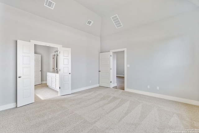 unfurnished bedroom with high vaulted ceiling and light colored carpet