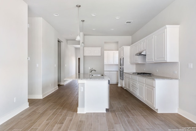 kitchen with light stone counters, an island with sink, light hardwood / wood-style flooring, white cabinetry, and stainless steel appliances