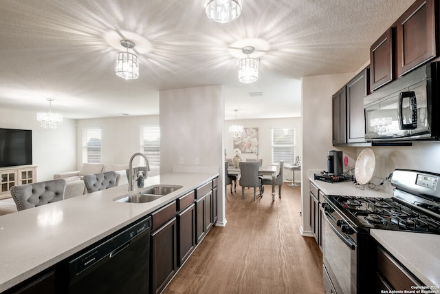 kitchen featuring light wood-type flooring, stainless steel range with gas stovetop, sink, decorative light fixtures, and dishwasher