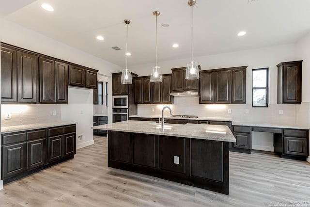 kitchen featuring an island with sink, hanging light fixtures, light hardwood / wood-style floors, stainless steel appliances, and light stone countertops