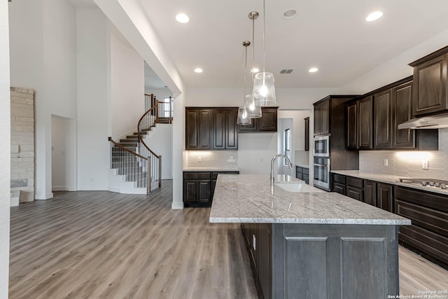 kitchen with hanging light fixtures, an island with sink, appliances with stainless steel finishes, and dark brown cabinetry