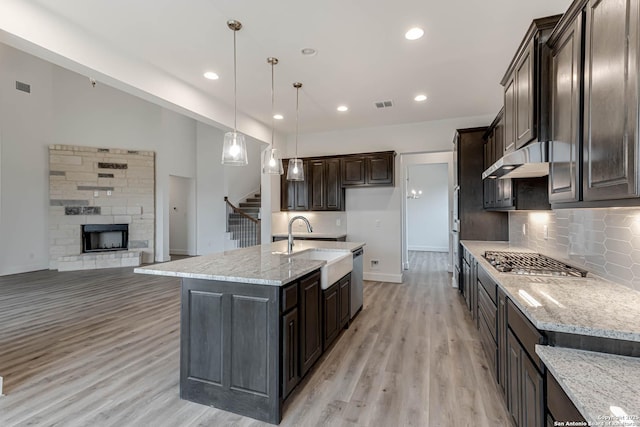 kitchen with decorative light fixtures, an island with sink, sink, light stone countertops, and dark brown cabinets