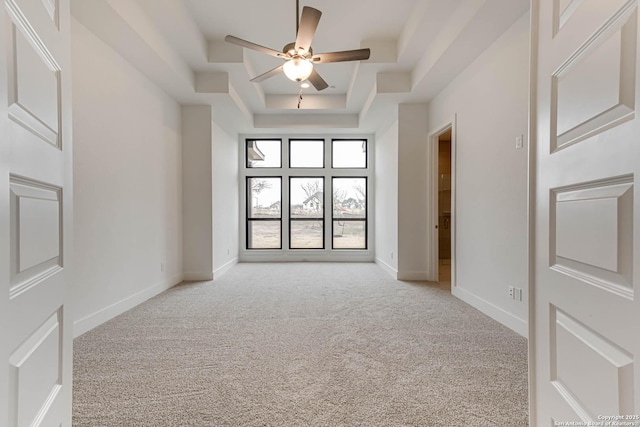 carpeted empty room with a tray ceiling, ceiling fan, and a high ceiling