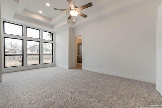 carpeted empty room with ceiling fan, a tray ceiling, and a towering ceiling