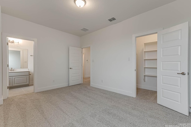 unfurnished bedroom featuring light carpet, a spacious closet, ensuite bath, and a closet