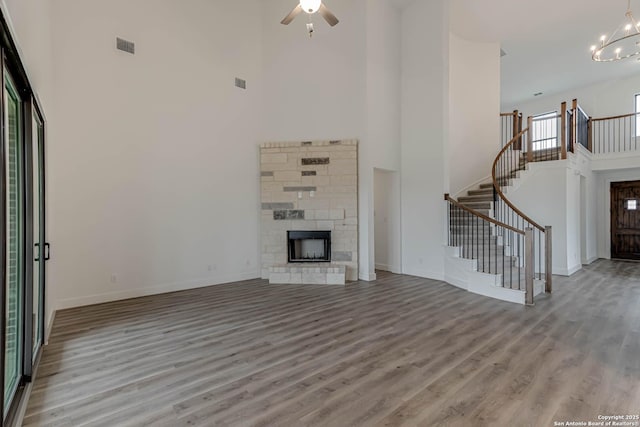 unfurnished living room with a stone fireplace, light wood-type flooring, ceiling fan with notable chandelier, and a towering ceiling