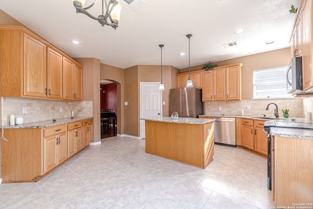 kitchen with tasteful backsplash, light stone counters, hanging light fixtures, appliances with stainless steel finishes, and a center island