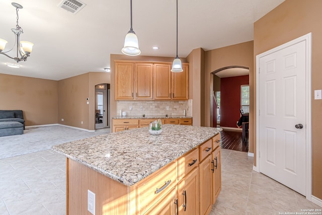 kitchen with pendant lighting, tasteful backsplash, a kitchen island, a notable chandelier, and light stone countertops