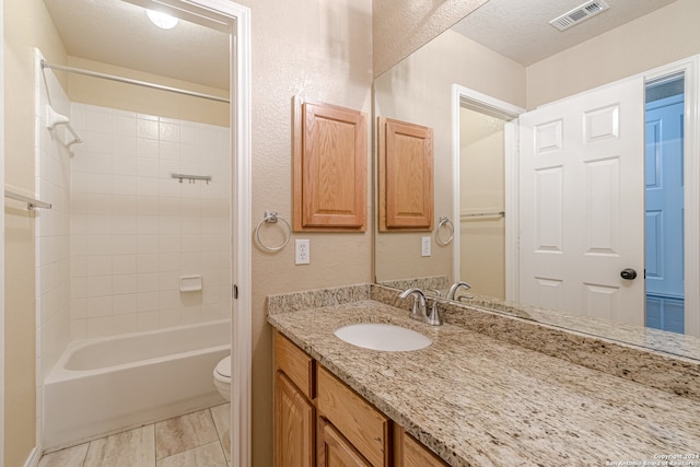 full bathroom with vanity, toilet, tiled shower / bath, and a textured ceiling