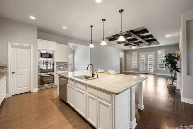 kitchen with dark wood-type flooring, sink, light stone counters, stainless steel appliances, and an island with sink