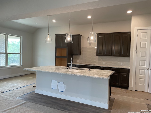 kitchen with an island with sink, light stone countertops, decorative backsplash, sink, and vaulted ceiling