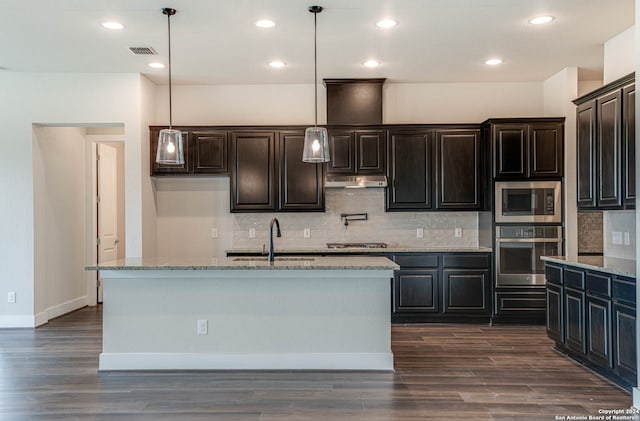 kitchen featuring sink, stainless steel appliances, decorative light fixtures, and a center island with sink