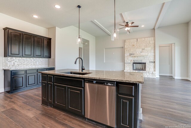 kitchen featuring a center island with sink, sink, stainless steel dishwasher, a fireplace, and dark hardwood / wood-style flooring