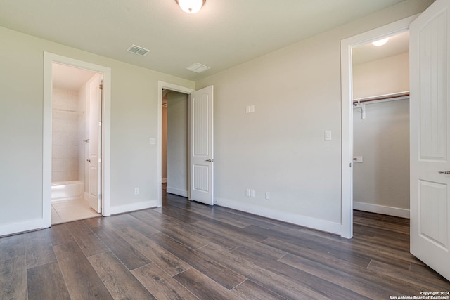 unfurnished bedroom featuring a spacious closet, ensuite bath, a closet, and dark wood-type flooring