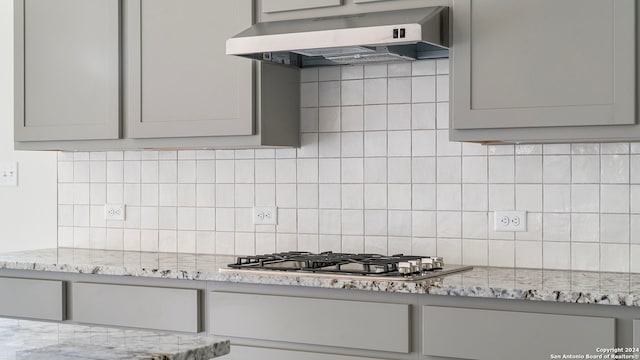 kitchen featuring tasteful backsplash, stainless steel gas stovetop, wall chimney range hood, gray cabinets, and light stone countertops