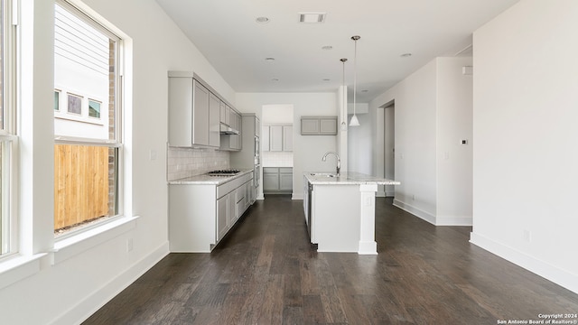 kitchen featuring tasteful backsplash, decorative light fixtures, gray cabinets, sink, and a kitchen island with sink