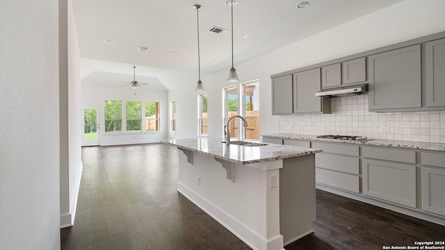 kitchen featuring a kitchen bar, an island with sink, decorative backsplash, sink, and ceiling fan