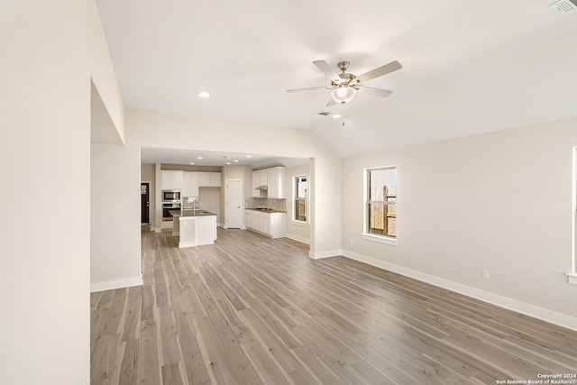 unfurnished living room with ceiling fan, vaulted ceiling, and light wood-type flooring