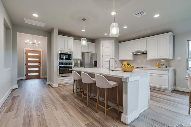 kitchen with appliances with stainless steel finishes, under cabinet range hood, tasteful backsplash, white cabinets, and light wood-style flooring