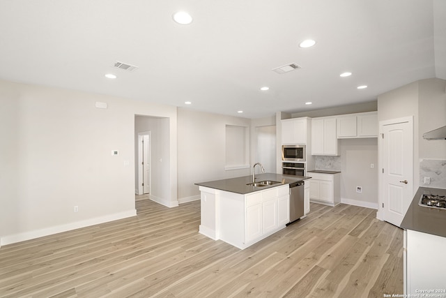 kitchen with appliances with stainless steel finishes, sink, an island with sink, white cabinets, and light hardwood / wood-style flooring