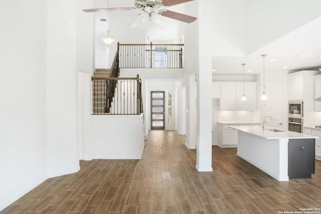 kitchen with pendant lighting, dark hardwood / wood-style floors, stainless steel appliances, an island with sink, and white cabinets