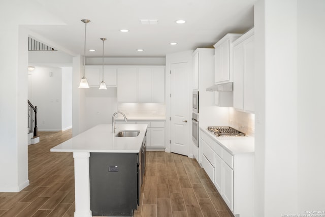 kitchen with white cabinets, pendant lighting, sink, a kitchen island with sink, and light hardwood / wood-style flooring