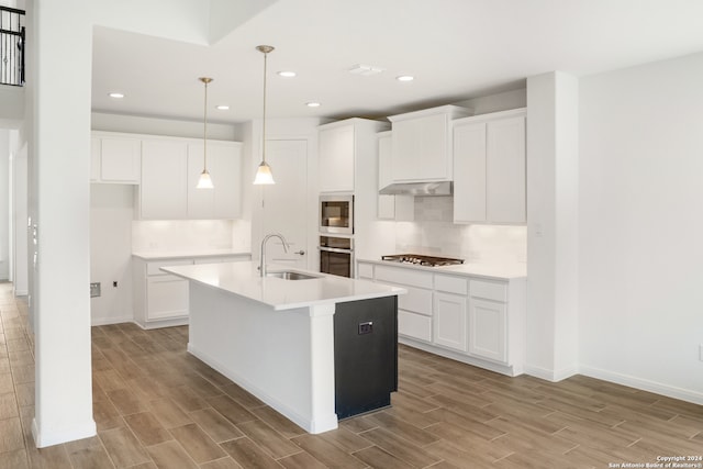 kitchen featuring appliances with stainless steel finishes, light wood-type flooring, sink, and an island with sink