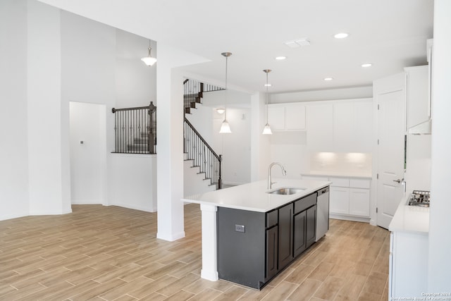 kitchen with decorative light fixtures, a kitchen island with sink, light hardwood / wood-style floors, and white cabinets