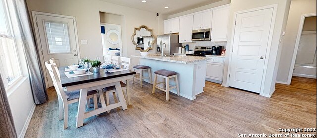 kitchen with light hardwood / wood-style floors, white cabinets, appliances with stainless steel finishes, and a kitchen island with sink