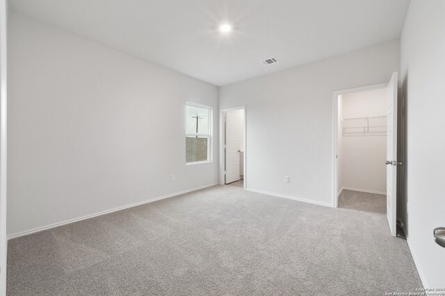 unfurnished bedroom featuring a closet, a walk in closet, and light carpet