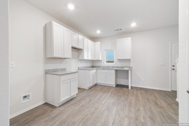 kitchen with white cabinets, light hardwood / wood-style flooring, sink, and light stone countertops